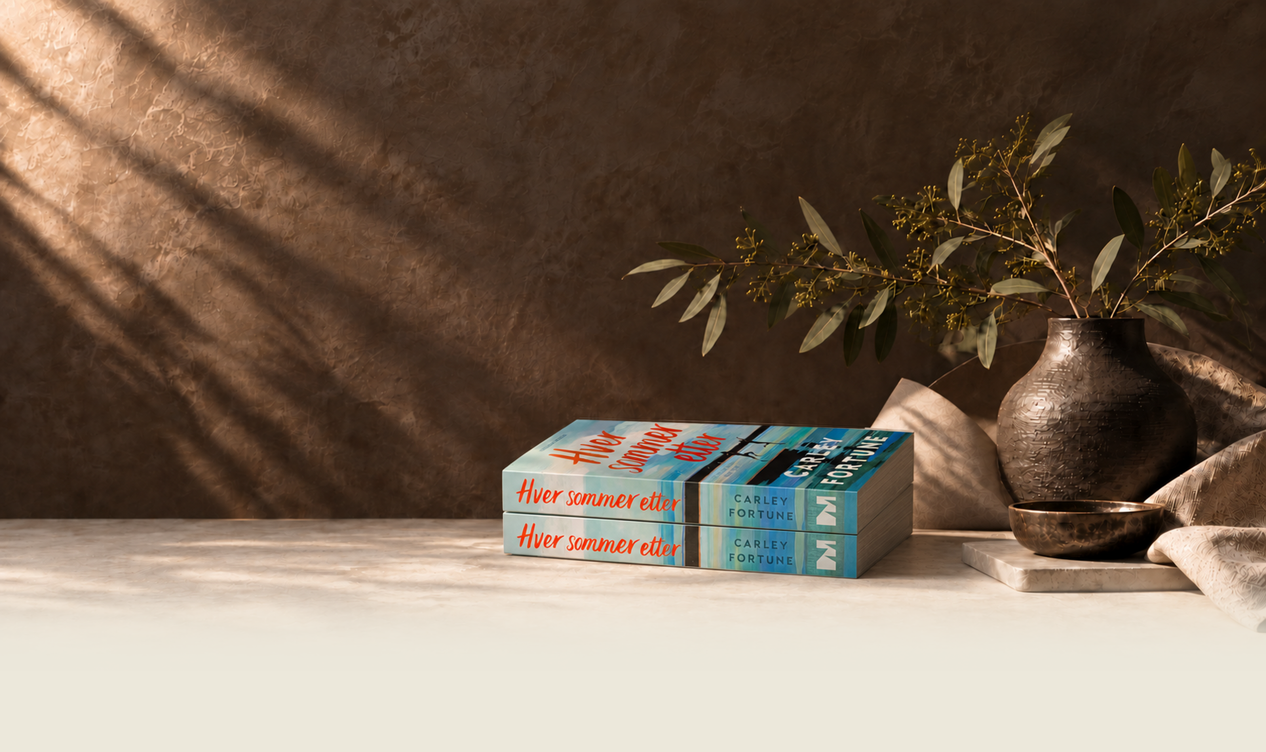 To eksemplarer av Hver sommer etter av Carley Fortune på et mørkt bord med potteplante og skål, korrigert lysere bunn